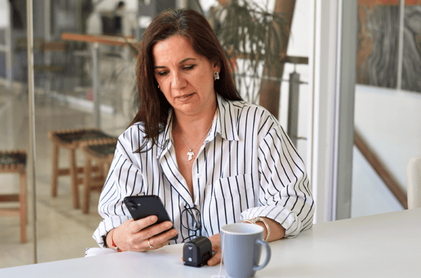 Mujer consultando el resultado de glucosa en la app de GLUCUBE desde el móvil, con el dispositivo médico no invasivo sobre la mesa
